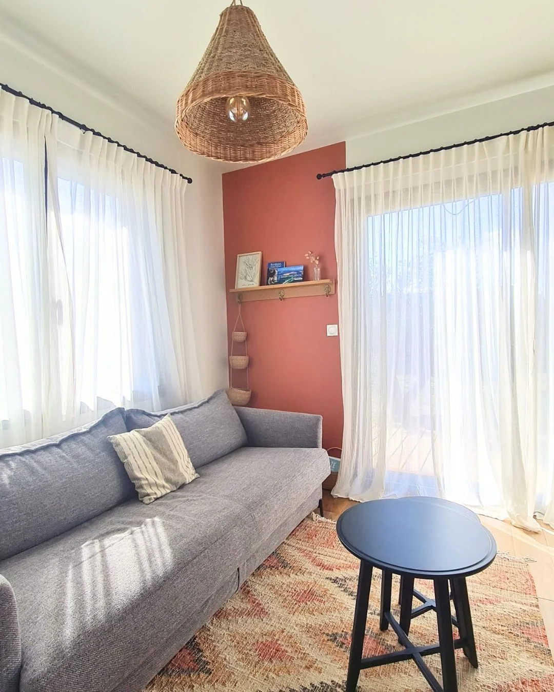 Rénovation d'un studio de 16m² à Saint-Médard-en-Jalles : salon avec canapé-lit gris, mur peint partiellement en terracotta avec étagères en bois et panier en osier