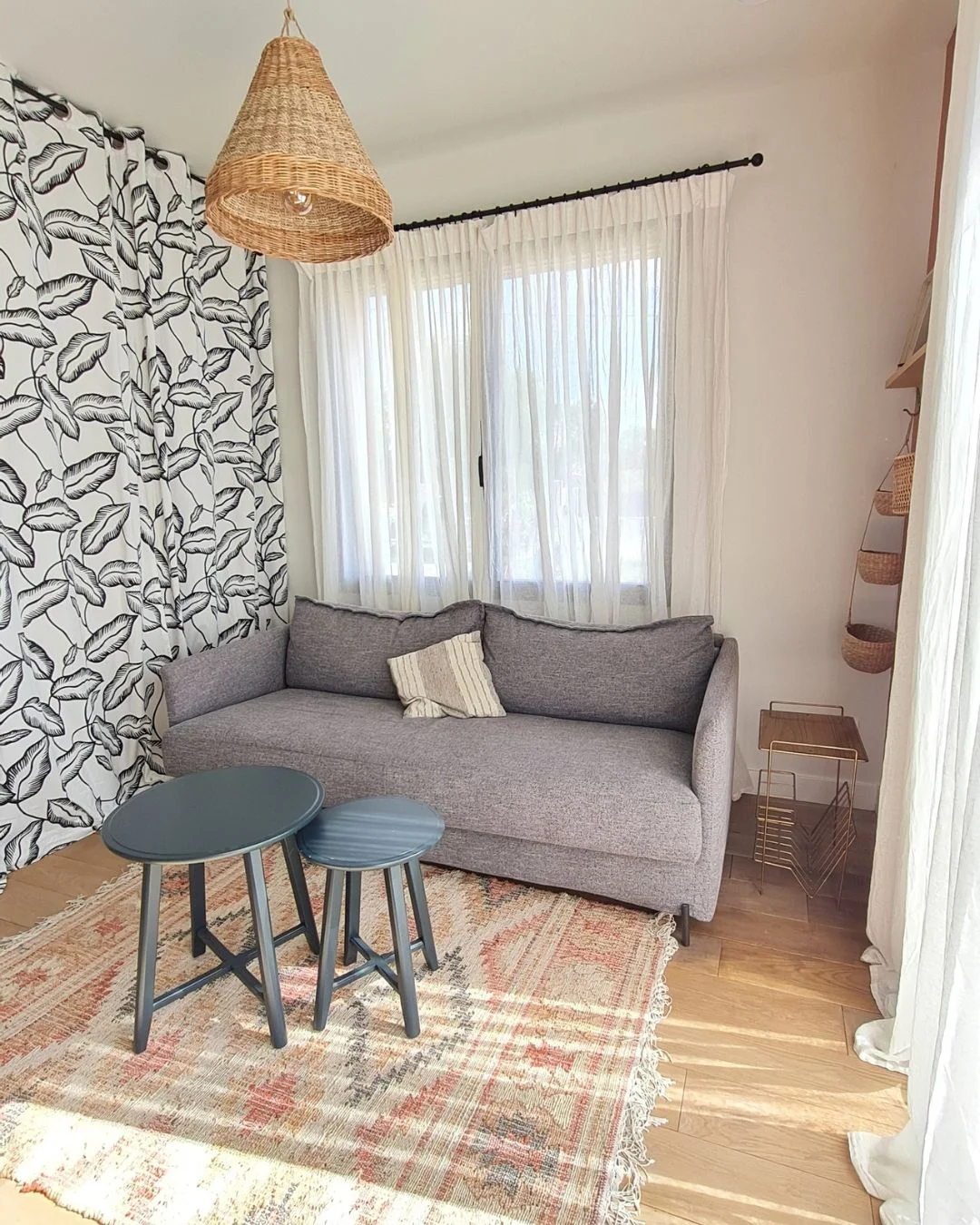 Rénovation d'un studio de 16m² à Saint-Médard-en-Jalles : salon avec canapé lit, gris, tables gigognes et dressing avec rideaux fleuris noir et blanc